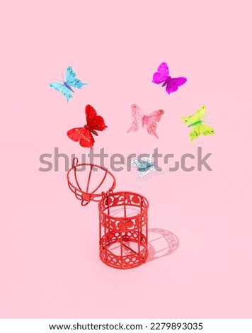 Open bird cage and colorful butterflies, creative aesthetic romantic spring inspired layout against pastel pink background. 