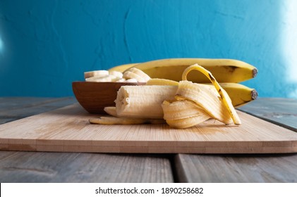 an open and bitten banana lies on a wooden board, from behind the cut bananas lie in a wooden cup, on the table