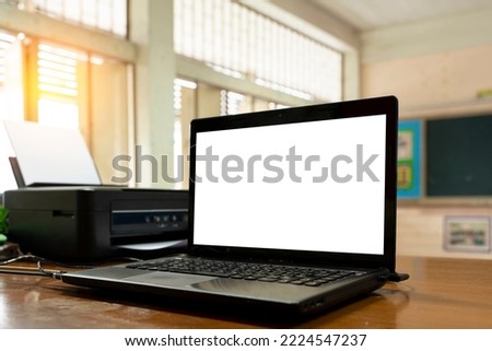 Open black laptop computer on a small chair table in classroom.Modern printer and laptop on table indoor.Creative designer desktop with blank white pc computer display. Front view.Advertising concept.