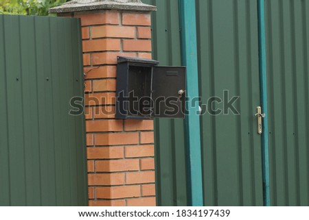an open black mailbox hangs on the brown bricks of the fence and the green metal wall in the street