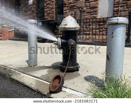 Open black and silver fire hydrant fitted with a city-approved spray cap to conserve water sprinkling water onto the street on a hot summer day in Harlem, New York City