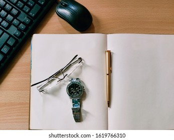 Open Blank Diary on computer table. Keyboard and mouse on a side. Specs, Hand Watch and pen top of the diary.