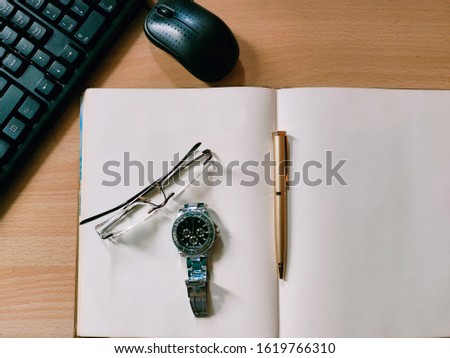 Open Blank Diary on computer table. Keyboard and mouse on a side. Specs, Hand Watch and pen top of the diary.