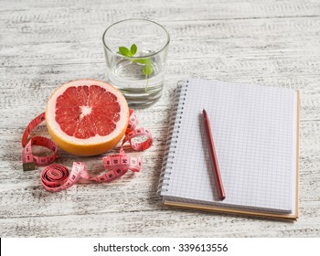 Open a blank Notepad, a grapefruit, a glass of water and measuring tape on a light wooden table. The concept of a healthy lifestyle, healthy food, diet - Powered by Shutterstock