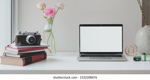 Open blank screen laptop computer with camera with roses vase and coffee cup on white wooden table 