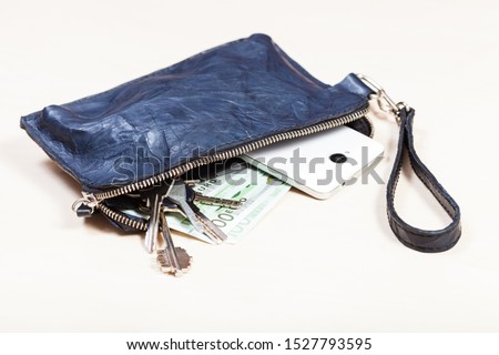 open blue leather wristlet purse bag with bunch of keys, smartphone and euro banknotes on pale brown table
