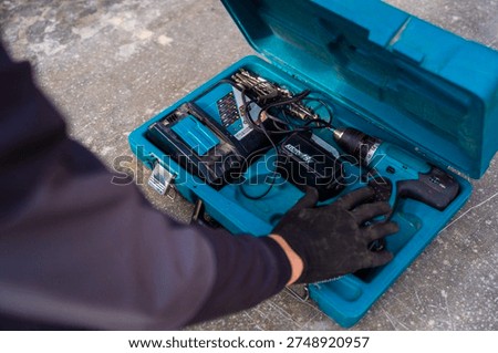 Open blue toolbox containing cordless drill, battery pack, charger and drill bits, top view of portable power tool set.