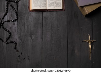 Open Book Of Bible And Crucifix On Dark Table, Top View. Flat Lay Image Of New Testament, Cross And Rosary On Old Black Background