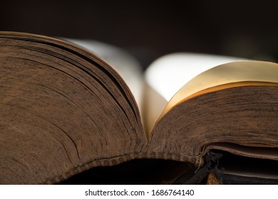 Open book or bible with a pattern in the edge of the pages with gold-like atmosphere and stitched or sewn binding. Black background, narrow depth of field