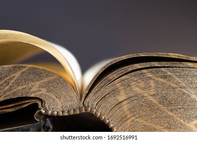 Open book or bible with a pattern in the edge of the pages with gold-like atmosphere and stitched or sewn binding. Dark background, narrow depth of field