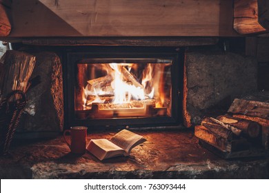 Open book by the Fireplace with Christmas ornaments. Open storybook lying on a wooden bench by the fireside. Cozy relaxed magical atmosphere in a chalet house decorated for Christmas. Holiday concept.