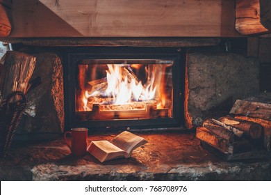 Open book by the Fireplace with Christmas ornaments. Open storybook lying on a wooden bench by the fireside. Cozy relaxed magical atmosphere in a chalet house decorated for Christmas. Holiday concept.