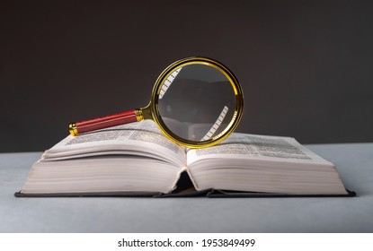 Open book closeup with turning pages and magnifying loupe. Textbook in hard cover on table. Studying and research concept.