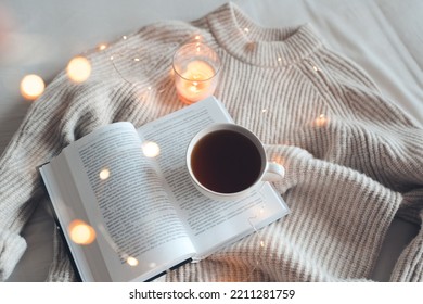 Open Book With Cup Of Coffee In Bed With Knit Cloth Sweater Over Glow Christmas Lights At Night. Top View. Good Morning. 