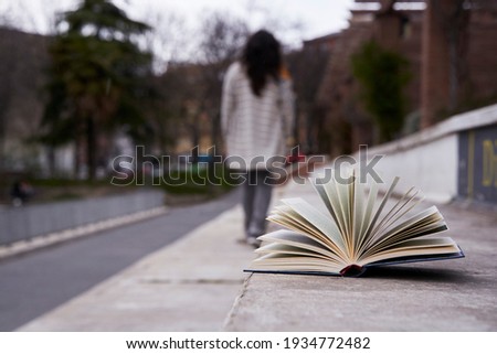 Open book forgotten on a stone seat and a woman walking away unfocused.
