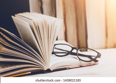 An open book with glasses on a wooden table against the background of a set of books, vintage toning. Literature, learning concept - Powered by Shutterstock