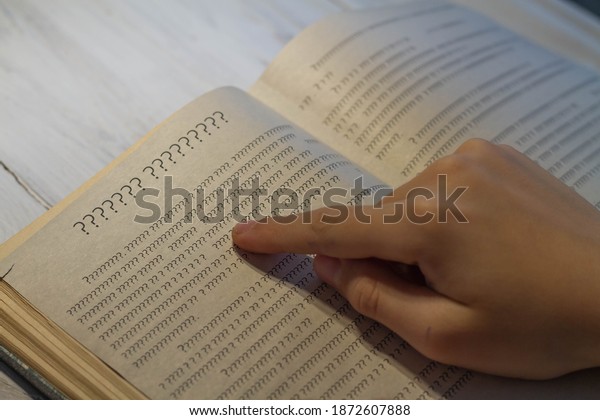 An open book with an\
incomprehensible text of question marks, a person tries to read the\
book.