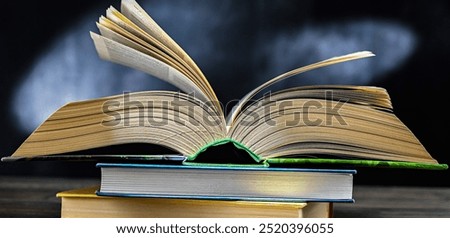 An open book lying on a stack of other books.