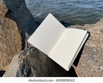 Open book, notebook or diary lies on the stones, sunny summer day. Mockup photo with empty white pages for text or advertising. Blue sky, rough rocks and stones.