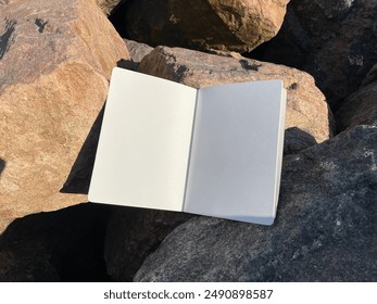 Open book, notebook or diary lies on the stones, sunny summer day. Mockup photo with empty white pages for text or advertising. Blue sky, rough rocks and stones.