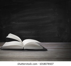 Open book on table in front of blackboard - Shutterstock ID 1018078507