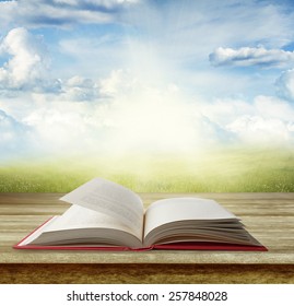 Open book on table in front of grass and sky