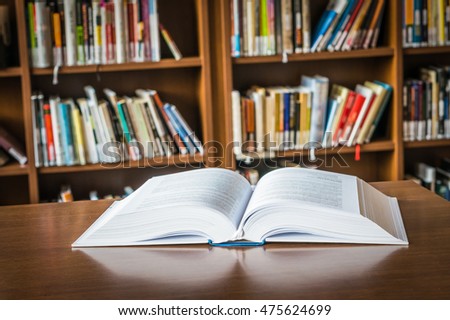 Open book on the table in a library and bookshelf in the background