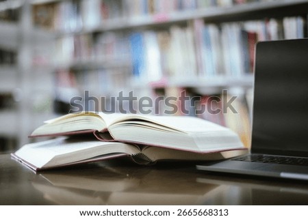 An open book with a stack of books on the table in the library beside a laptop, representing the concept of basic education.