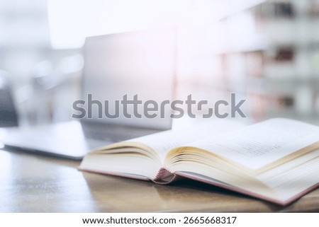 An open book with a stack of books on the table in the library beside a laptop, representing the concept of basic education.