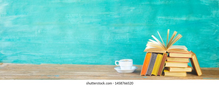 Open Book And Stack Of Multicolored Hardback Books With A Cup Of Coffee, Reading Education, Literature Concept. Panoramic, Mock Up, Banner Template, Free Copy Space