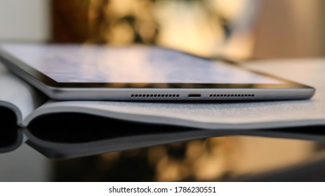 An Open Book And Tablet On A Glass Black Coffee Table. Blurred Bokeh Background, Close-up. Light Interior With Sunlight, Sunset, Bokeh.