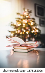 Open Book And Two Books On The Table. In The Background A Christmas Tree And Christmas Lights. Christmas Atmosphere.