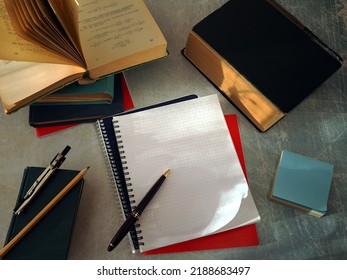 Open books and notebooks lie on the table. There is a pen on a clean notebook page. The concept of education, study, scientific work.