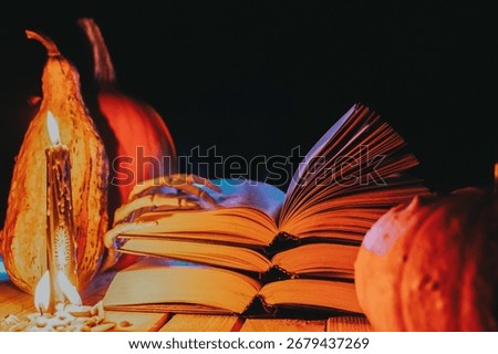 Open books stack, pumpkins, skeleton hand and black burning candles with blue smoke in the night.Fall Literature and Halloween Books. Autumn scary stories and fairy tales.
