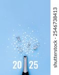 Open bottle of champagne on blue background decorated with silver star confetti and numbers 2025. New Year celebration or party. Selective focus, place for text