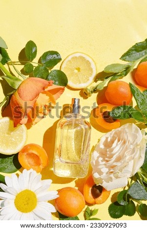Open bottle of perfume with rose, green leaves, apricot, lemon, chamomile, drops of water on the yellow background. Idea of sweet pure smell for young girls. Fruity and flowery perfume. Place for text