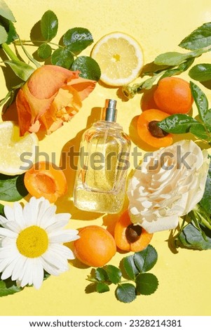 Open bottle of perfume with roses, green leaves, apricot, lemon, chamomile, drops of water on the yellow background. Fresh aroma. Idea of sweet pure smell for young girls. Fruity and flowery perfume