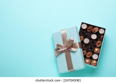 Open box of delicious chocolate candies on light blue background, flat lay. Space for text