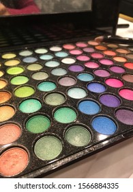 Open box of eye shadow in different colors with mirror for beautiful make-up. Small brush in blurred background.