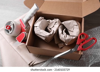Open box with wrapped items, adhesive tape, scissors, paper and bubble wrap on wooden table - Shutterstock ID 2160103729