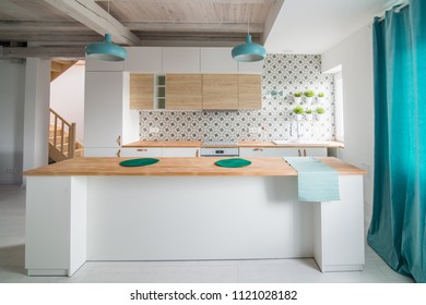 Open bright kitchen with white furniture. Island kitchen. Turquoise lamps and curtains. Modern, bright attic apartment.