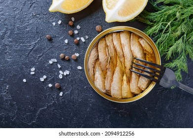 Open Can With Canned Baltic Smoked Sprats In Oil, One On Fork, With Lemon, Dill. Top View, Overhead, Flat Lay. Canned Food Concept.