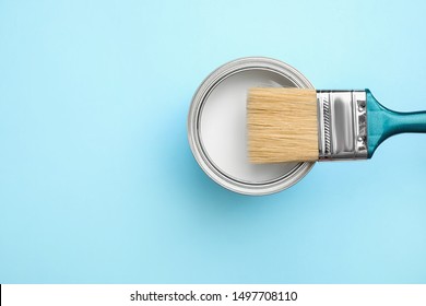 Open Can With White Paint And Brush On Blue Background, Top View. Space For Text