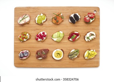 Open Canape Sandwiches And Bite Size Crostinis On A Wooden Serving Board. Party Food Crackers With Toppings Isolated On White.