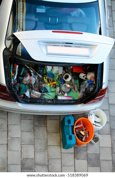 Open car trunk baggage\
compartment loaded with old work tools and junk on grey paving\
stone background