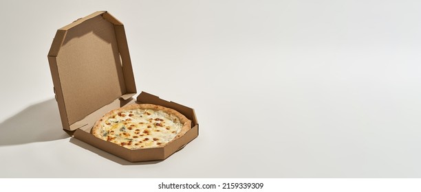 Open cardboard box with delicious and appetizing four cheese pizza. Unhealthy eating and fast food. Fresh baked high-calorie junk food for lunch and leisure. White background. Studio shoot. Copy space