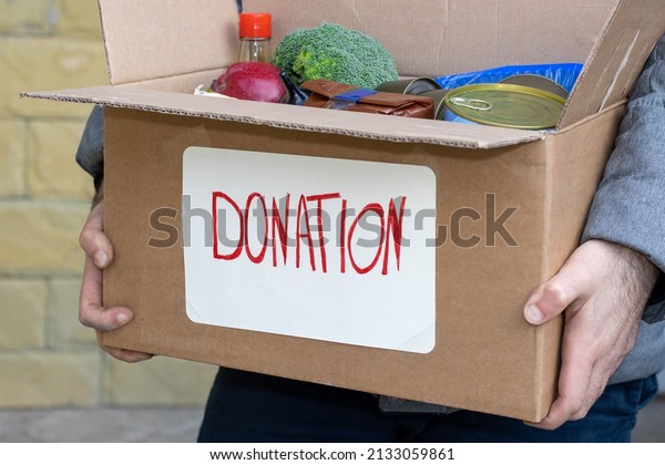 Open cardboard box\
with food for donation, on a car\'s seat or in a man\'s hands.\
inscription donation attached on the box. Volunteer for helping\
hungry people. delivery\
food.