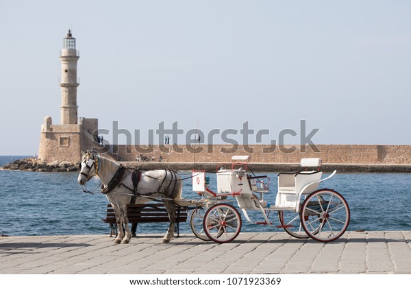 Open carriage and a horse in Chania harbor,\
cityscape, and medieval architecture of the touristic town. Crete,\
Greece landmarks. Sunny\
day.