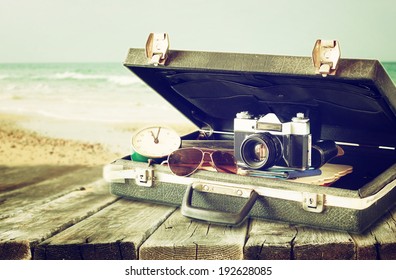 open case with old camera sunglasses and clock in front of seascape. filtered image.