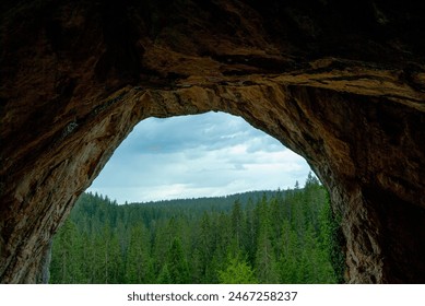 An open cave in Bosnia and Herzegovina reveals its towering walls, framed by the vibrant blue sky above and lush forest below, creating a captivating natural panorama. - Powered by Shutterstock